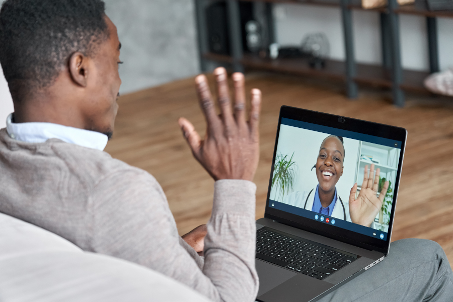 A man waves to his primary care doctor on his laptop screen via a telehealth appointment.